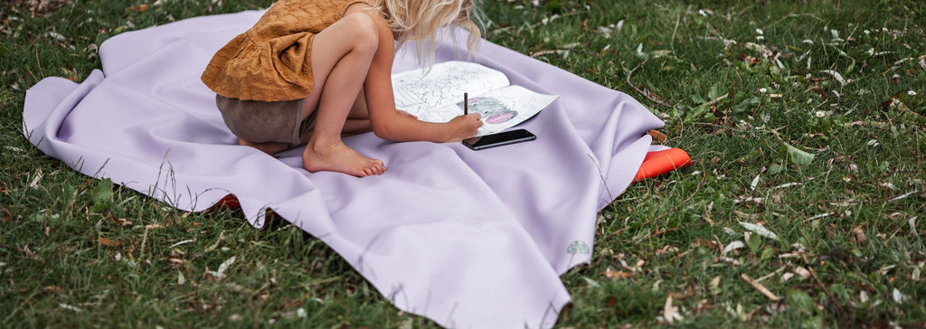 Studio Huske silicone play mat: a lilac mat laid flat on grass with a child drawing on it
