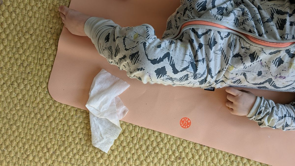 Peach silicone leather mat laid over a woven jute rug, a baby on the mat and a used wipe beside them