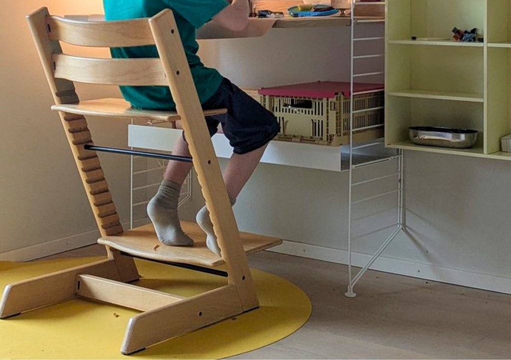 Child eating at a Stokke Tripp Trapp high chair with a yellow Studio Huske Roam Round silicone mat underneath