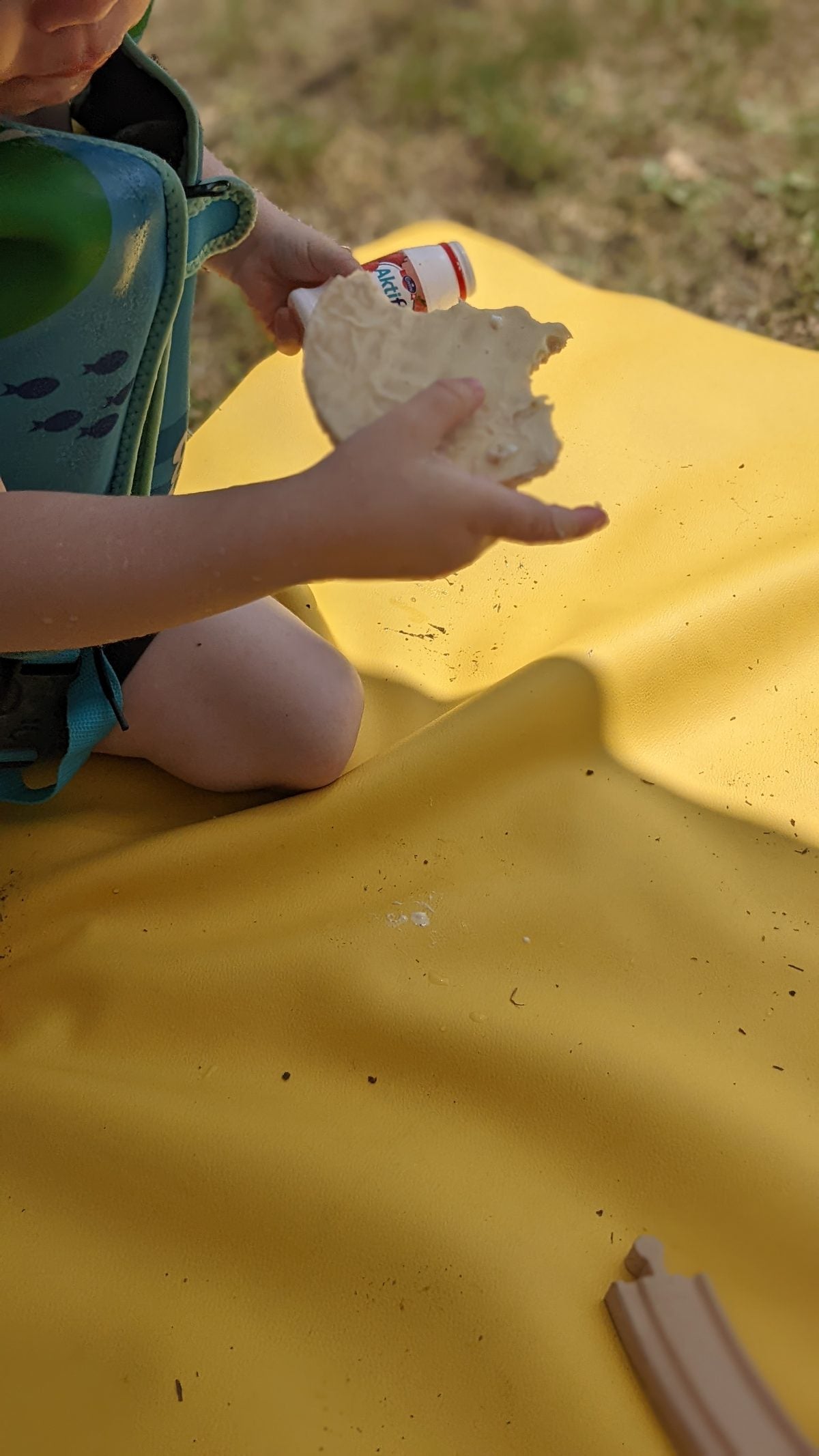Child snacking on a yellow Studio Huske silicone mat laid on outdoor grass