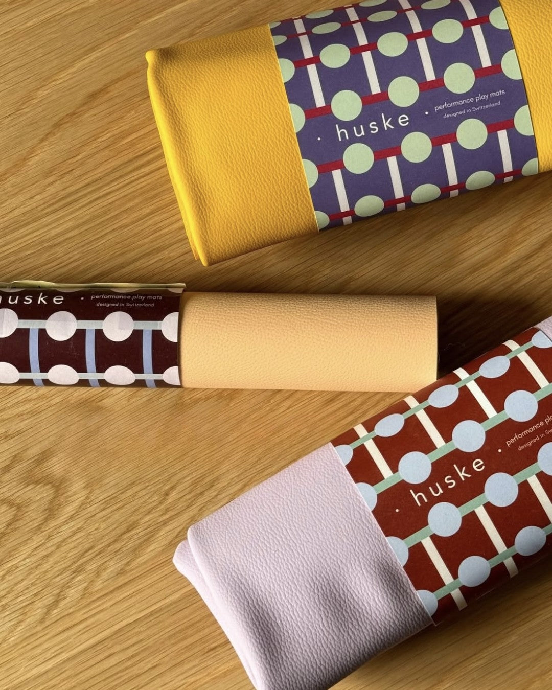 Studio Huske packaging: three rolled mats with illustrated belly bands in yellow, peach, and lilac