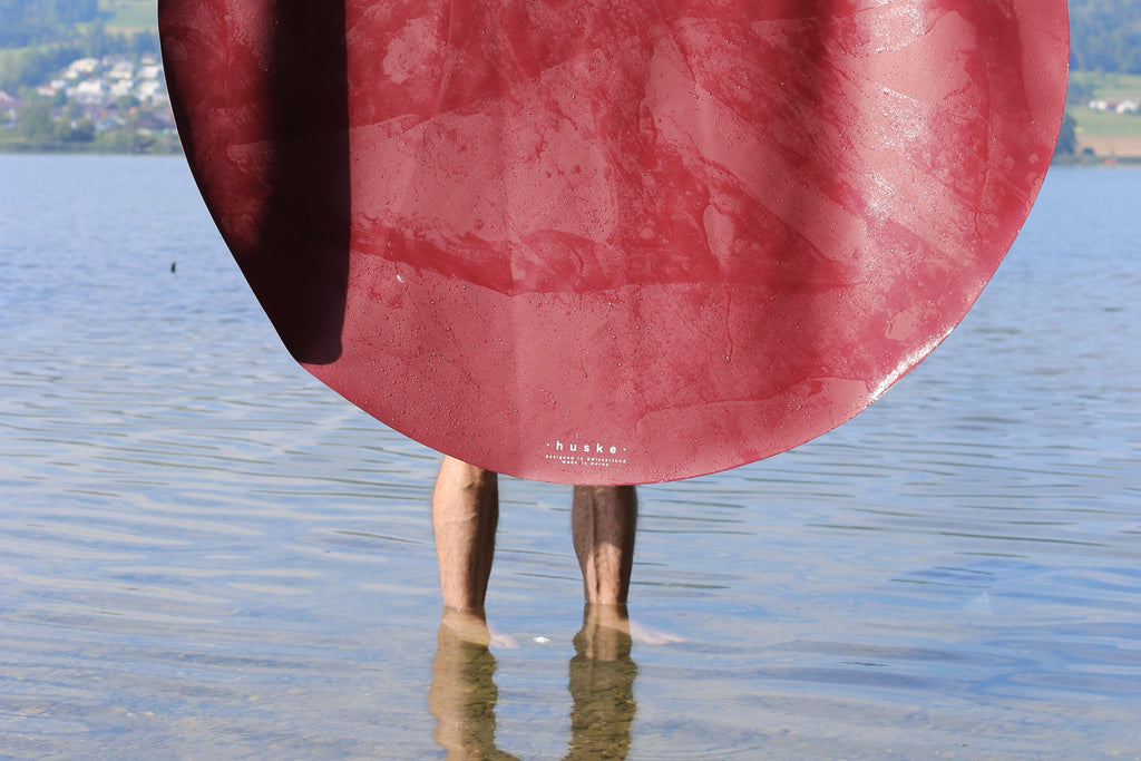 Studio Huske round play mat held dripping over a Swiss lake, hills behind