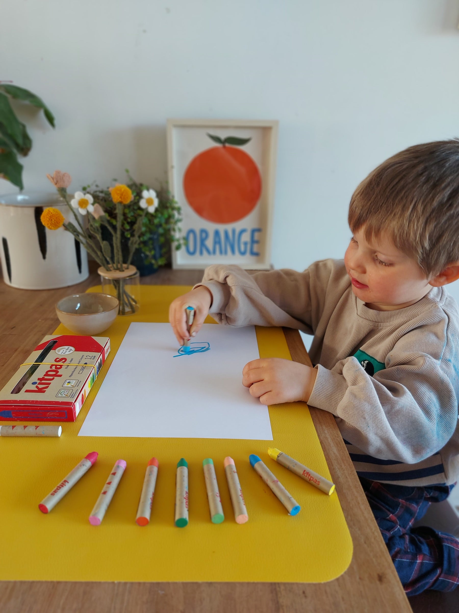 Toddler boy drawing with Kitpas crayons on mustard yellow Huske mat used as desk