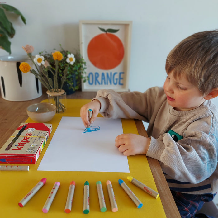Toddler boy drawing with Kitpas crayons on mustard yellow Huske mat used as desk