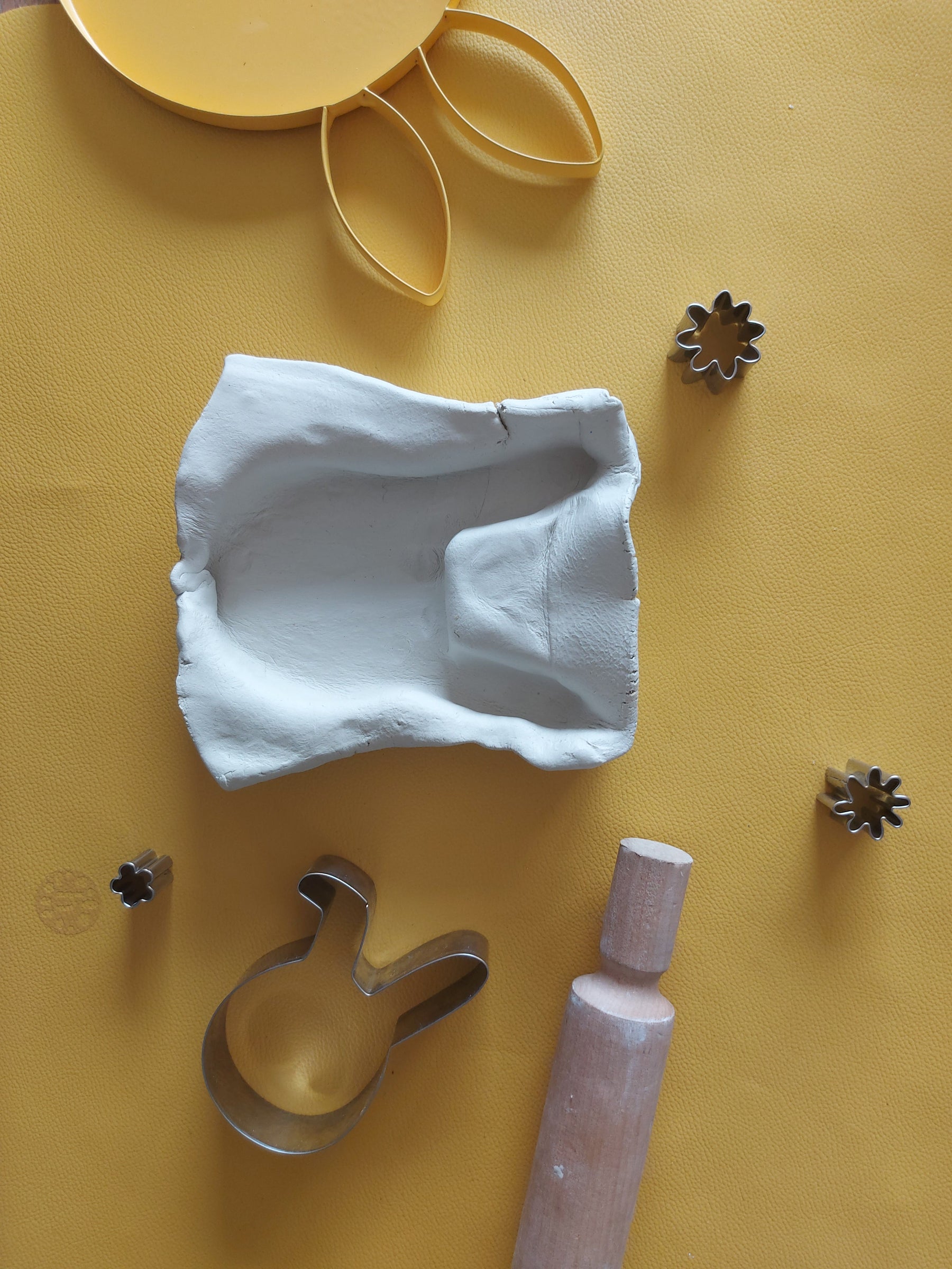 Flat lay on mustard yellow Huske mat with clay models and creative play items