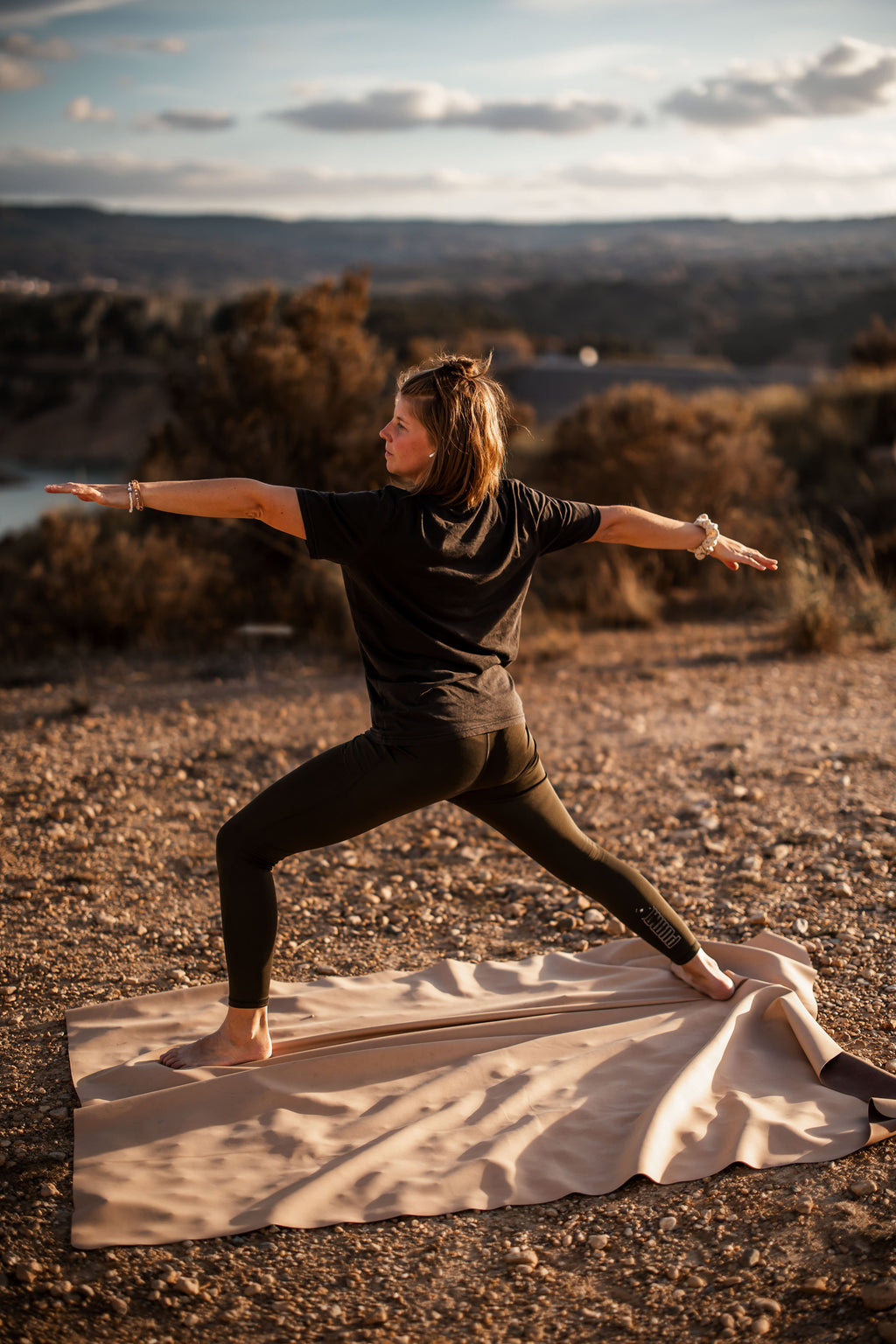 Woman in warrior yoga pose on Huske mat at golden sunset on hilltop