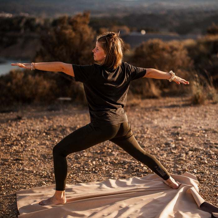 Woman in warrior yoga pose on Huske mat at golden sunset on hilltop