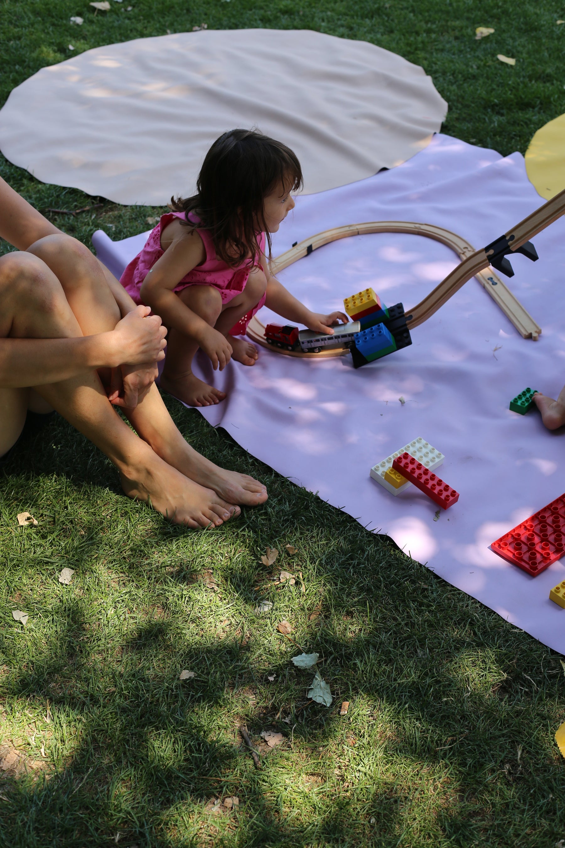 Adult and toddler playing with wooden train tracks and Duplo bricks on Huske mat in garden