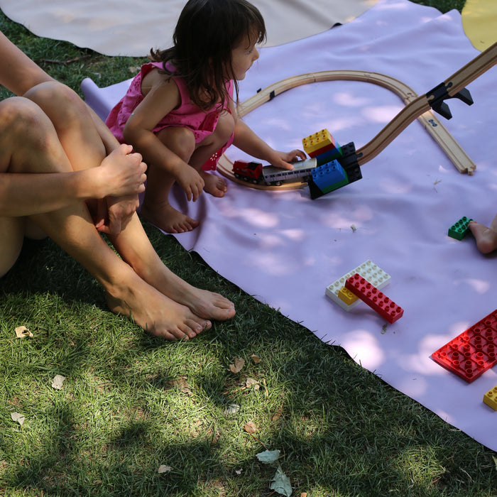 Adult and toddler playing with wooden train tracks and Duplo bricks on Huske mat in garden