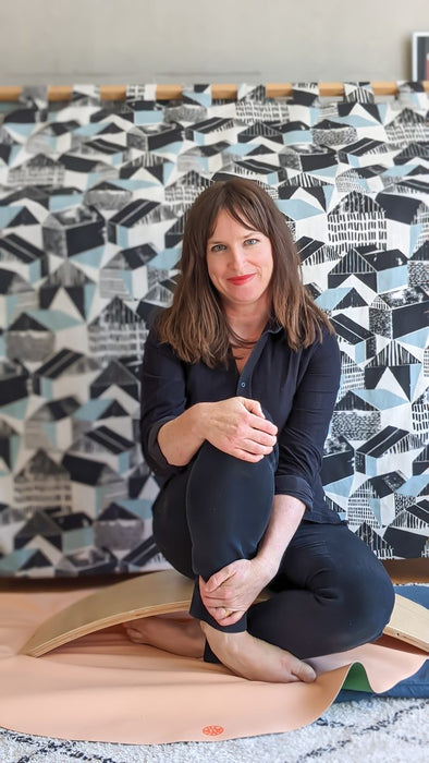Studio Huske founder Kate Gannon sitting on peach silicone mat surrounded by geometric artwork prints