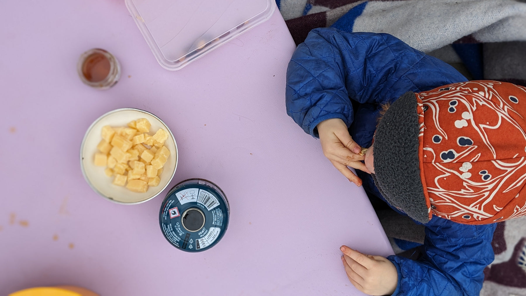 Overhead winter picnic scene with cheese and snacks on lavender Huske mat, Swiss Alps setting