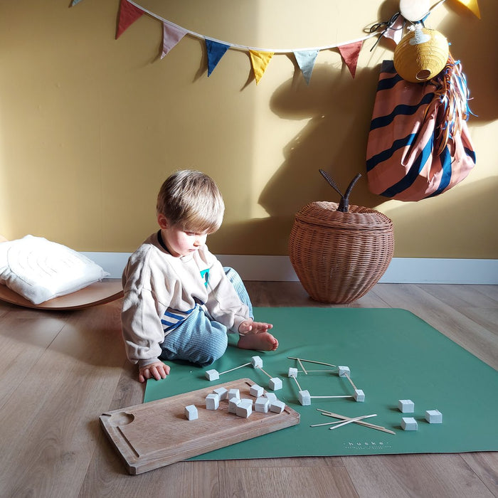 Toddler crafting on sage green Huske play mat in sunlit kids room with colourful bunting