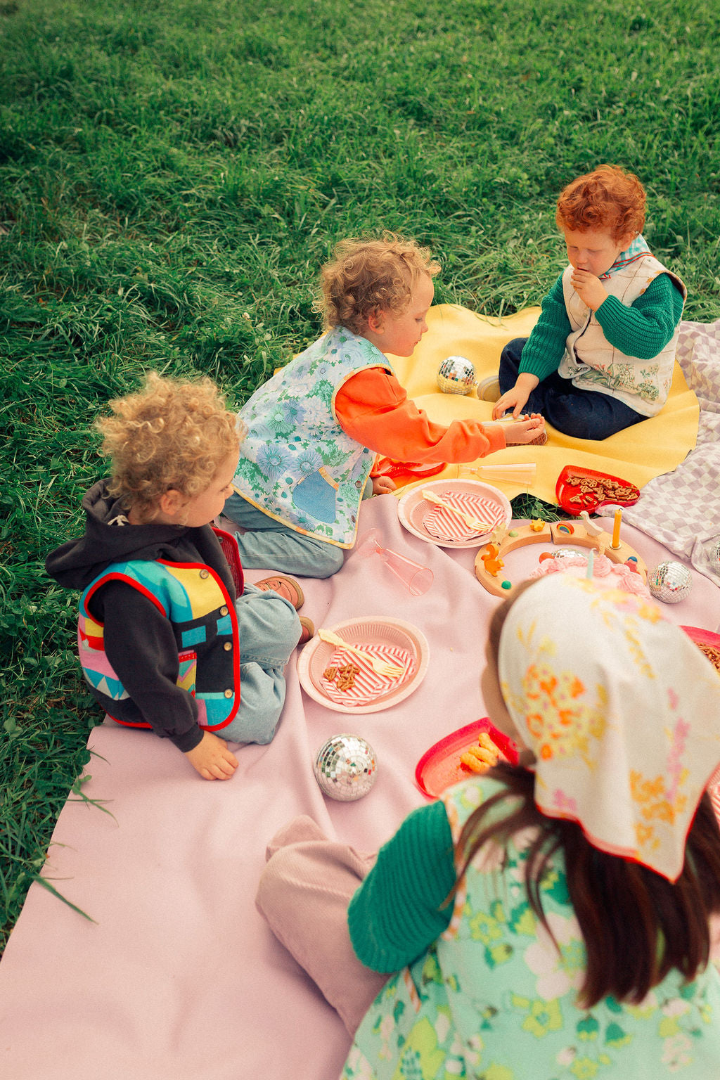 Group of children having outdoor picnic on pink and yellow Huske mats, Swiss countryside