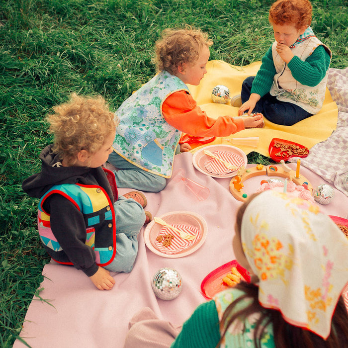 Group of children having outdoor picnic on pink and yellow Huske mats, Swiss countryside