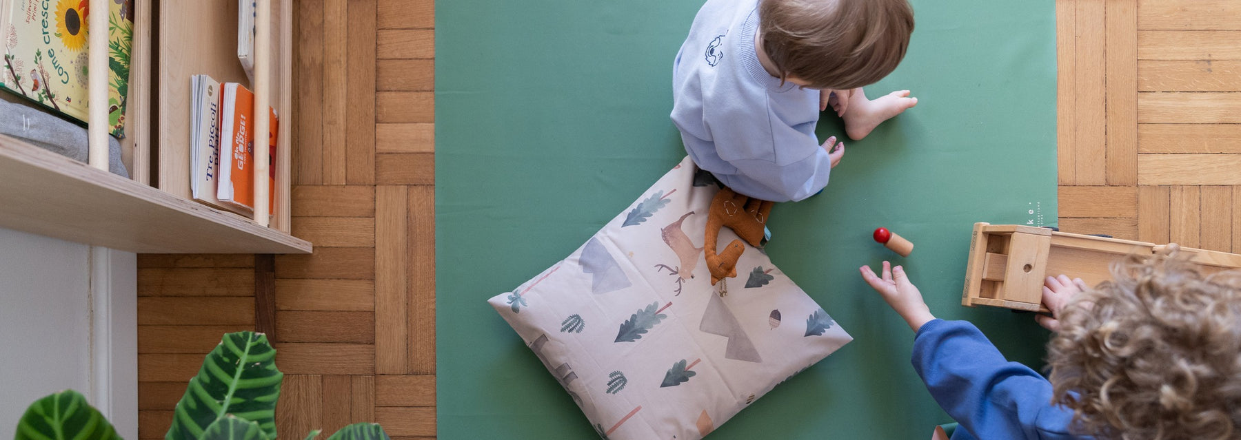 Studio Huske square play mat: green mat lying flat on a parquet floor while two children play with wooden toys