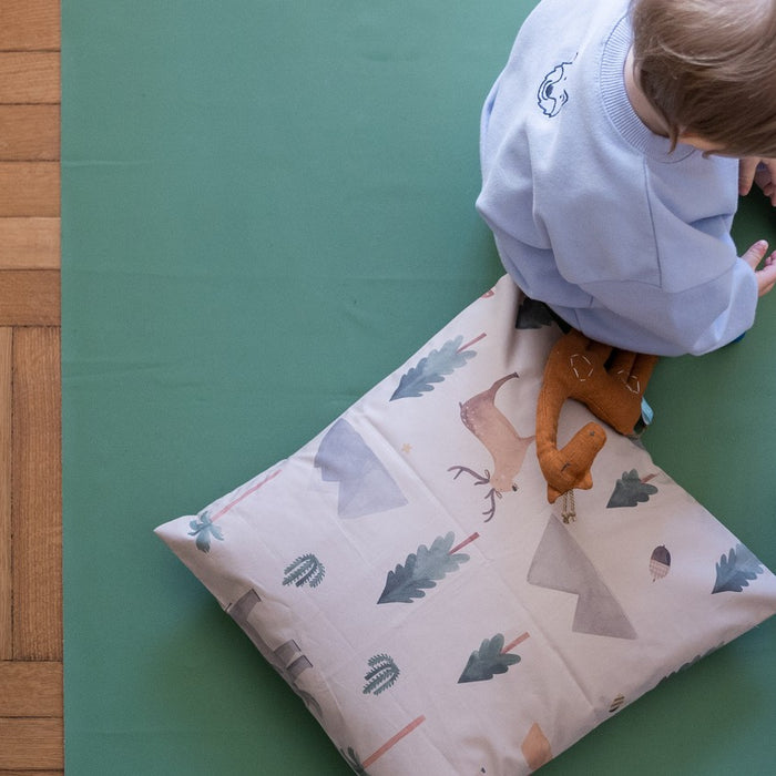 Studio Huske square play mat: green mat lying flat on a parquet floor while two children play with wooden toys