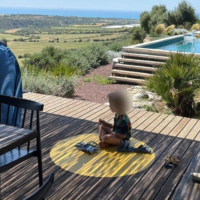 Runde gelbe Matte von Studio Huske: Kind auf einer Ferienterrasse unter einer Schilfpergola, mit Pool und Meerblick