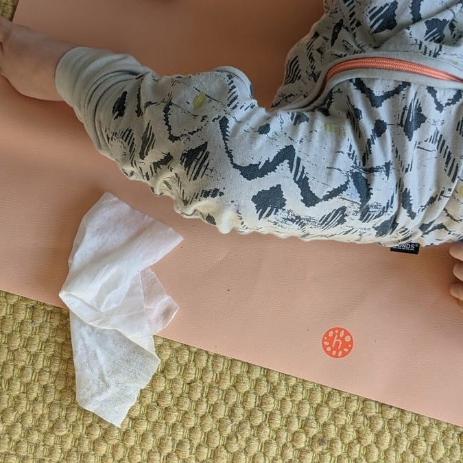Peach silicone leather mat laid over a woven jute rug, a baby on the mat and a used wipe beside them
