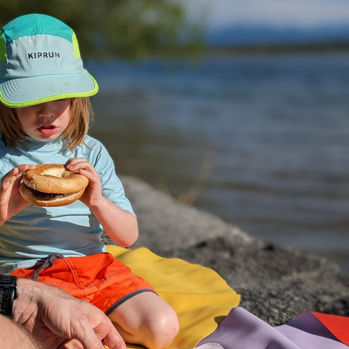 Father and toddler having a lakeside picnic in Switzerland on a yellow and a lavender silicone play mat by the water's edge