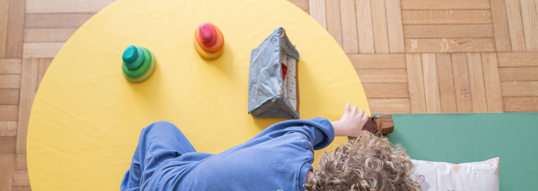 Studio Huske round play mat: child playing with wooden toys on a yellow mat on parquet