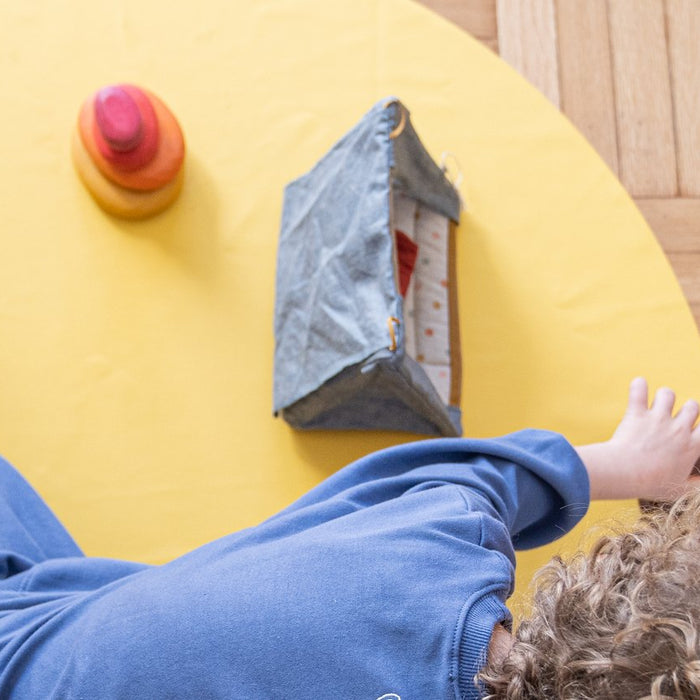 Studio Huske round play mat: child playing with wooden toys on a yellow mat on parquet
