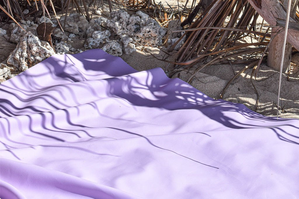 Purple Huske play mat on a sandy beach with palm frond shadows