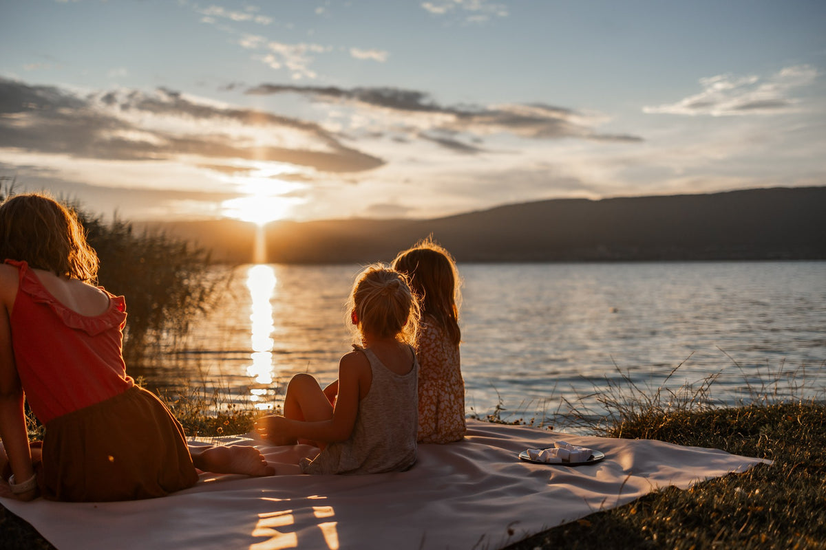 Family on beige silicone mat watching sunset by Swiss lake with mountain panorama