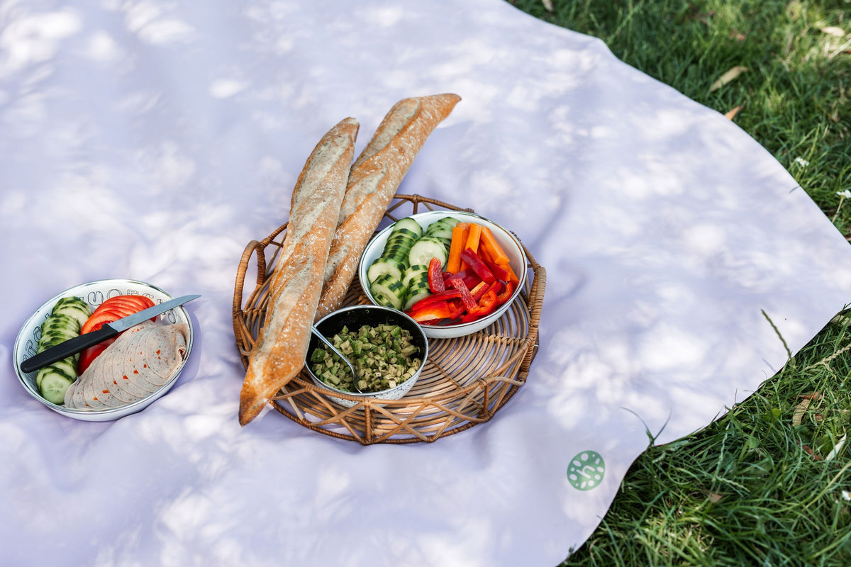 Studio Huske lavender silicone mat on grass with picnic spread of baguettes and hummus