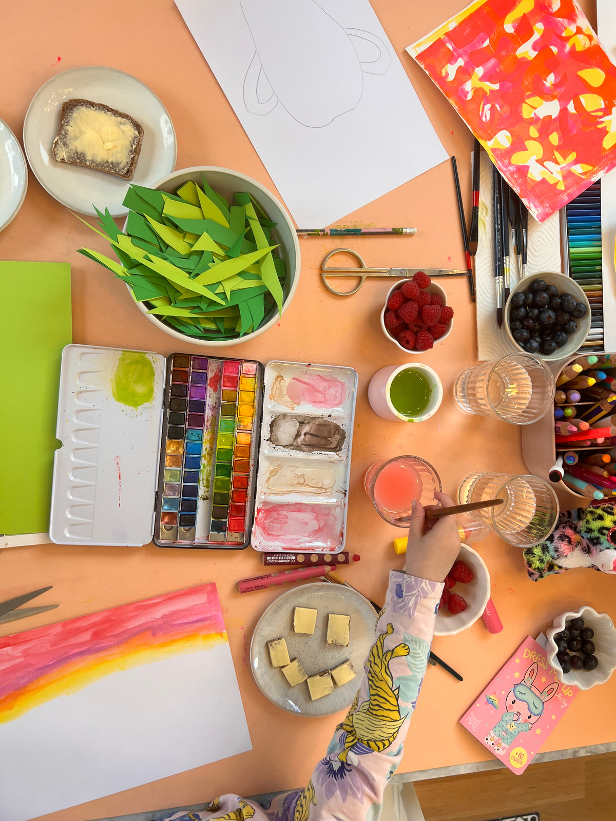 Studio Huske wipeable art mat — Overhead view of a creative art table covered with watercolor paints, paper cut leaves,