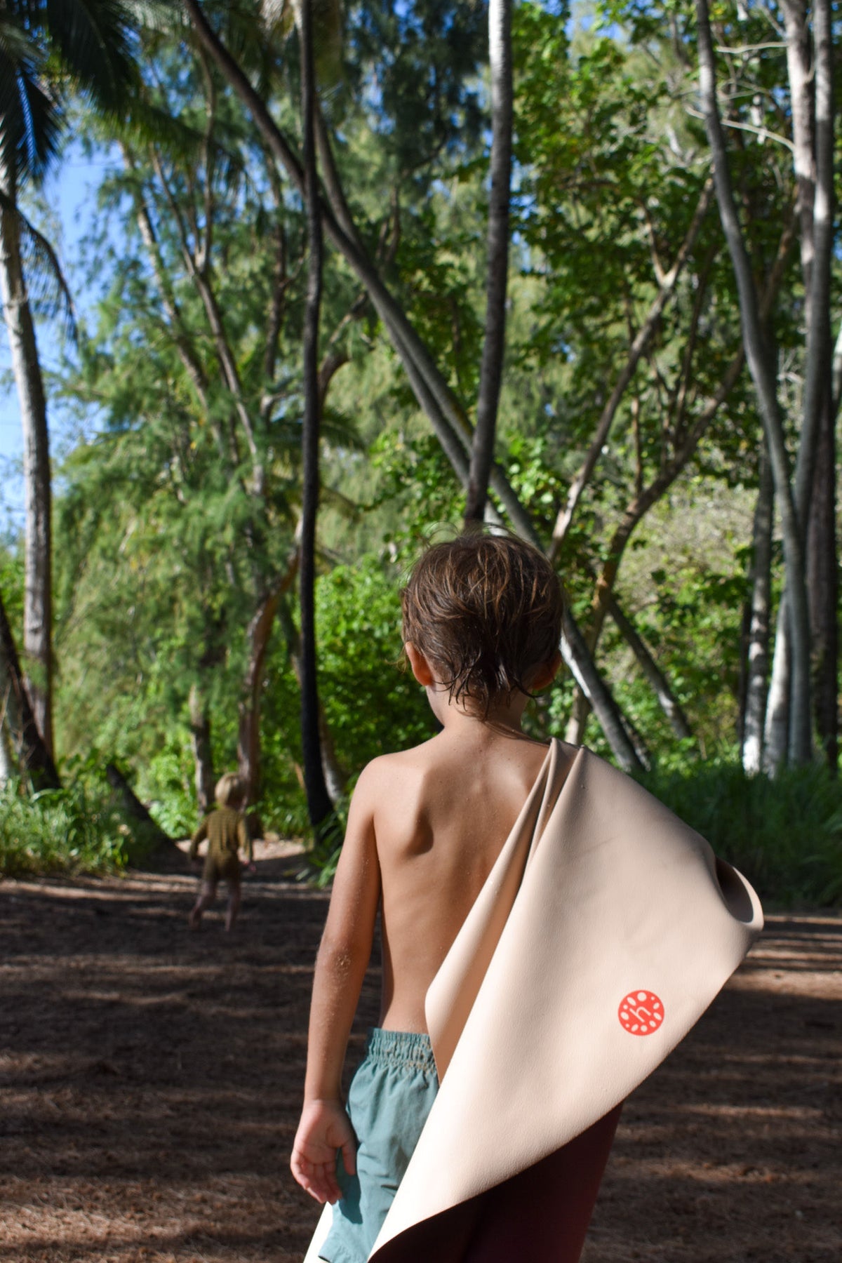 Studio Huske outdoor play mat — boy with wet hair carrying rolled blush mat through Hawaiian forest path