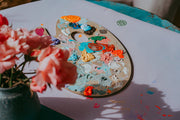 Studio Huske Wriggle Lilac/Red silicone changing mat and placemat, paint palette and flowers on the wipeable lilac mat