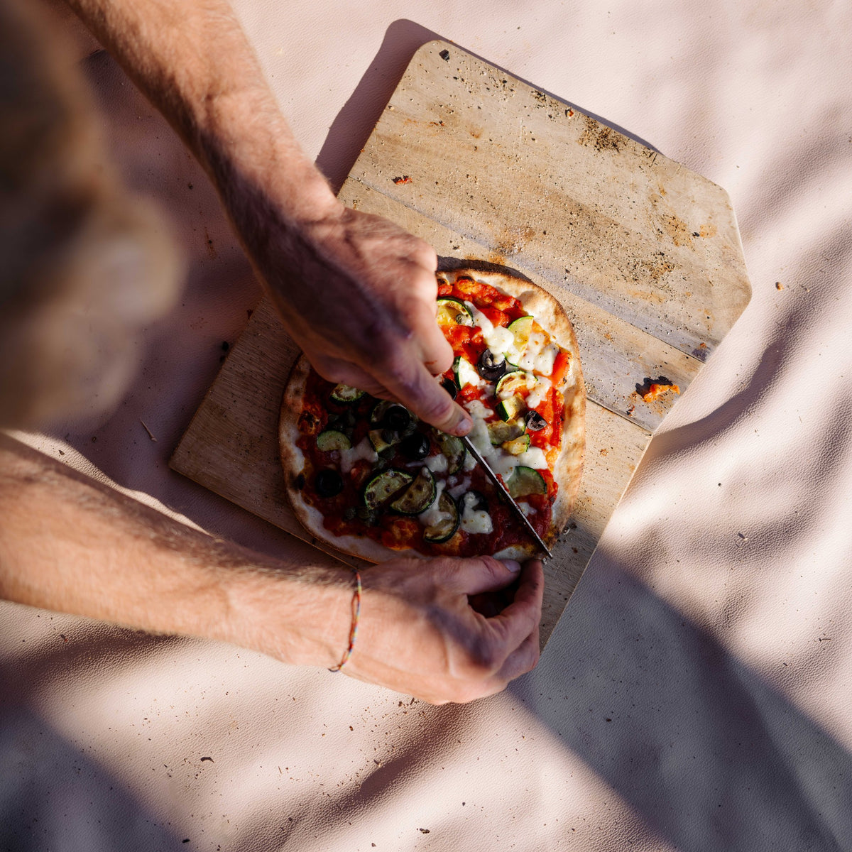 Explore Beige/Wine large round silicone play mat, hands slicing a pizza on a board on the beige mat
