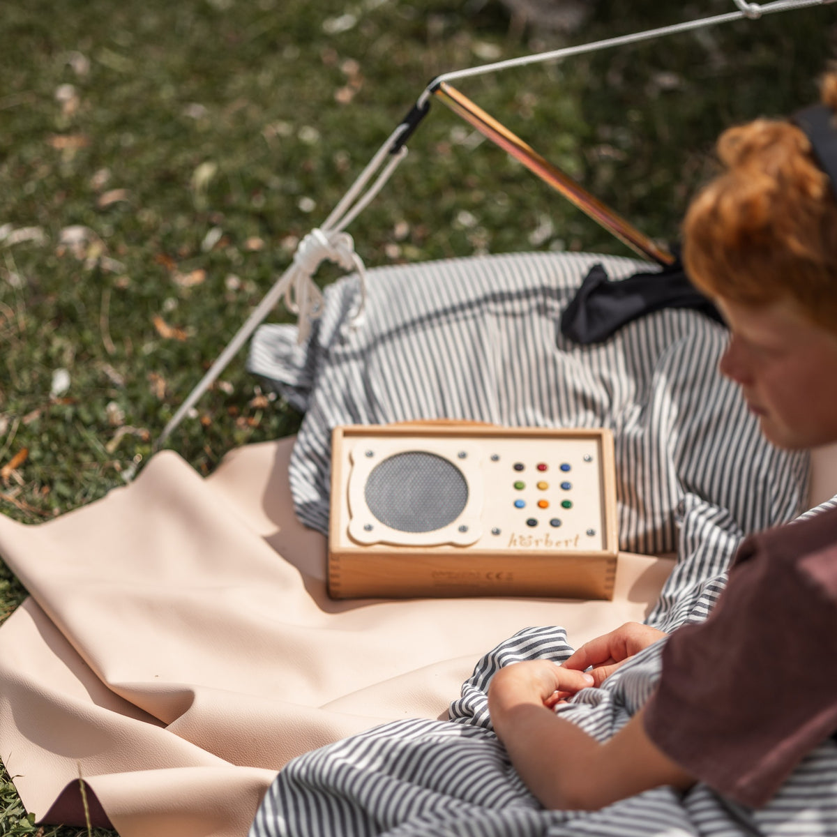 Explore Beige/Wine large round silicone play mat, child listening to a music box beside a tent on the beige mat