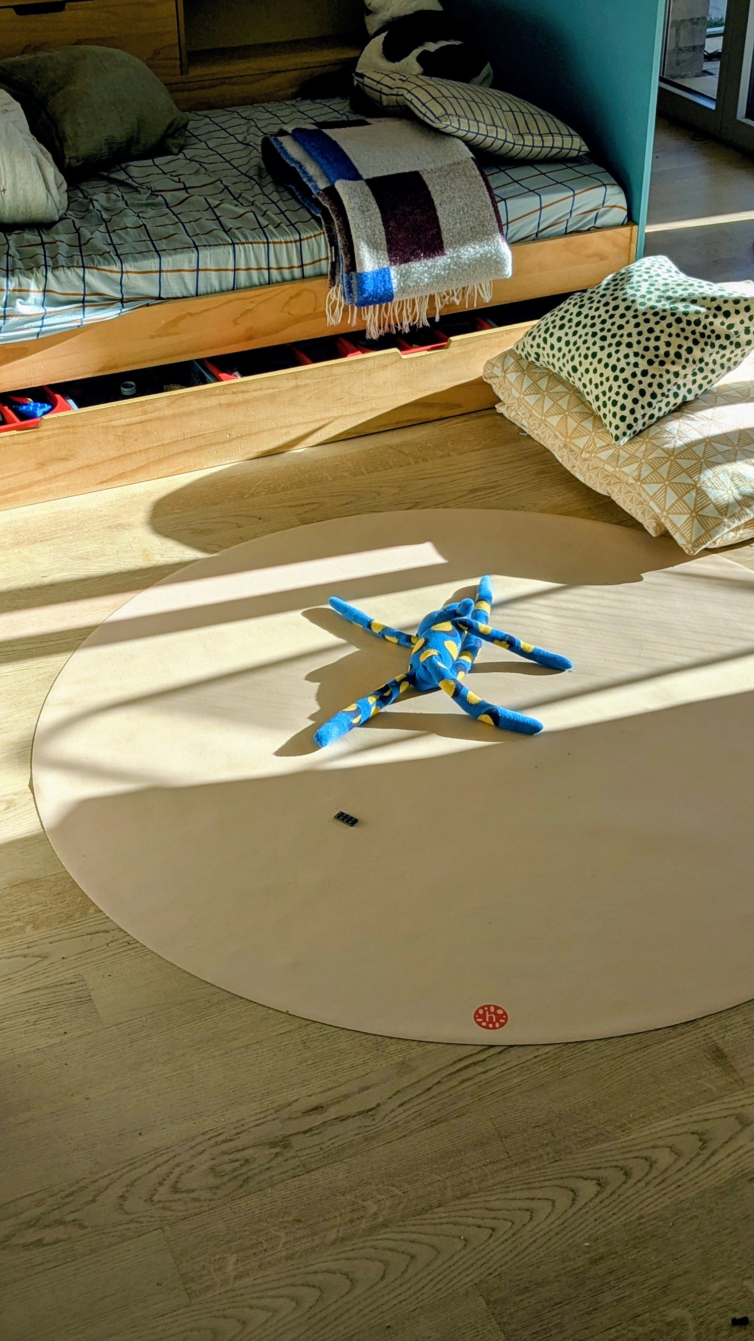 Studio Huske round play mat: wide view of the beige mat on a wooden floor in a child’s bedroom