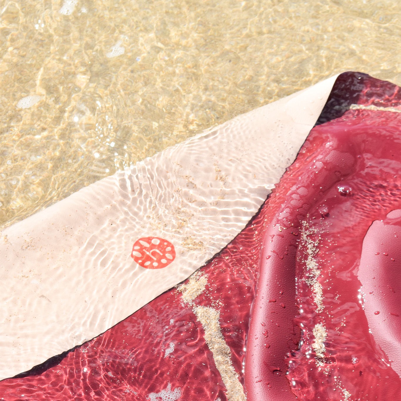 Explore Beige/Wine large round silicone play mat, blush sand huske mat partially submerged in shallow crystal clear ocean