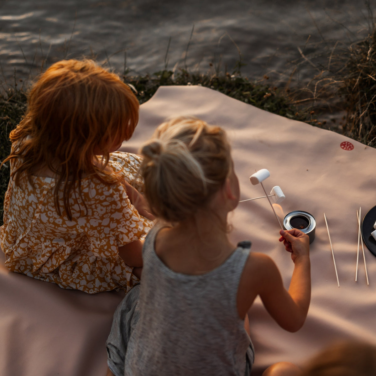 Gallivant XL Silikon-Picknickmatte in Beige/Weinrot, zwei Kinder rösten am Wasser Marshmallows auf der Matte