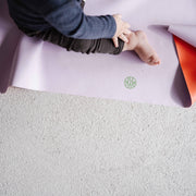 Roam Square Lilac/Red silicone craft mat, bare toddler foot on the lilac mat beside the logo