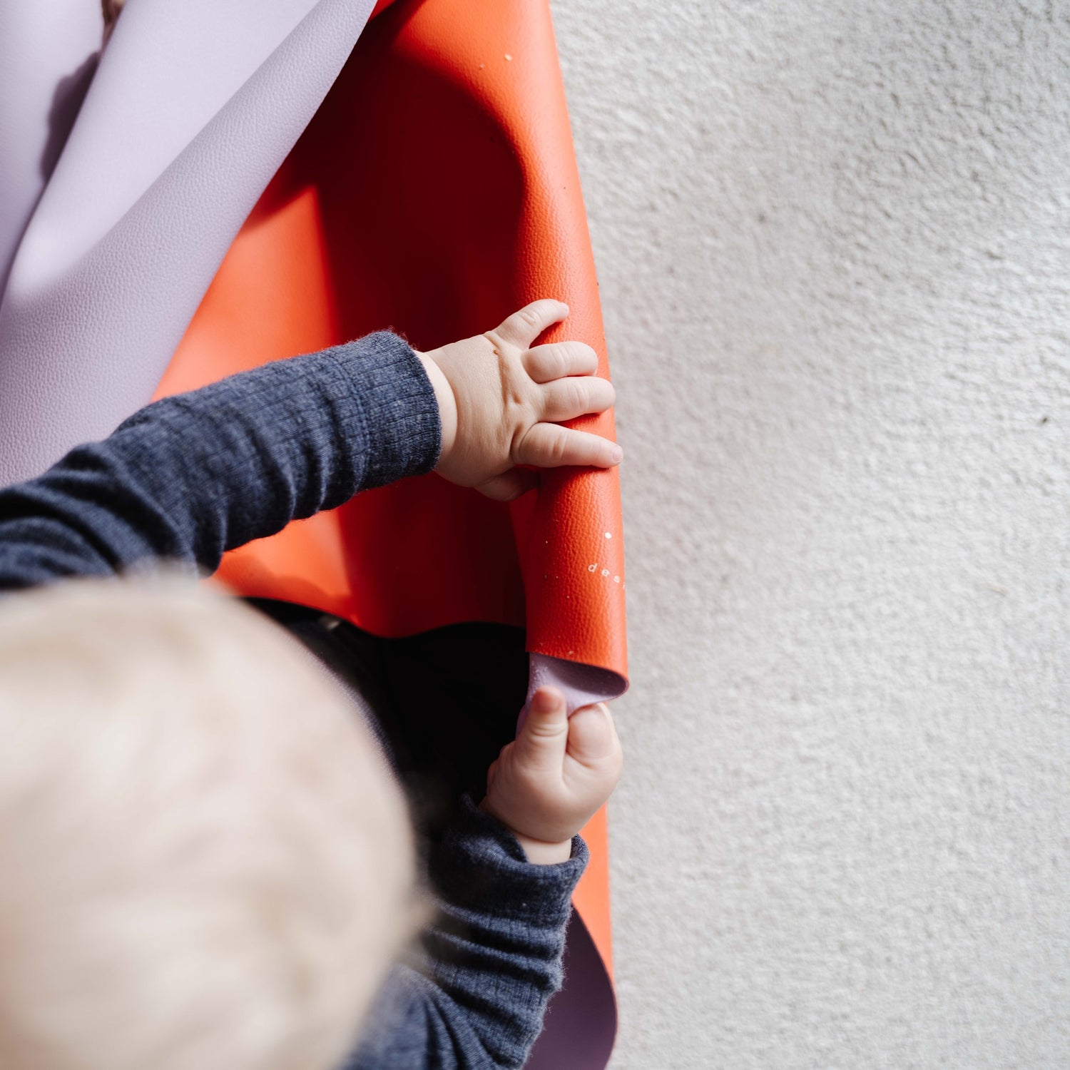 Roam Square Lilac/Red silicone craft mat, small hands gripping the rolled mat showing the red reverse