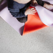 Roam Square Lilac/Red silicone craft mat, toddler lifting the mat to show the red underside
