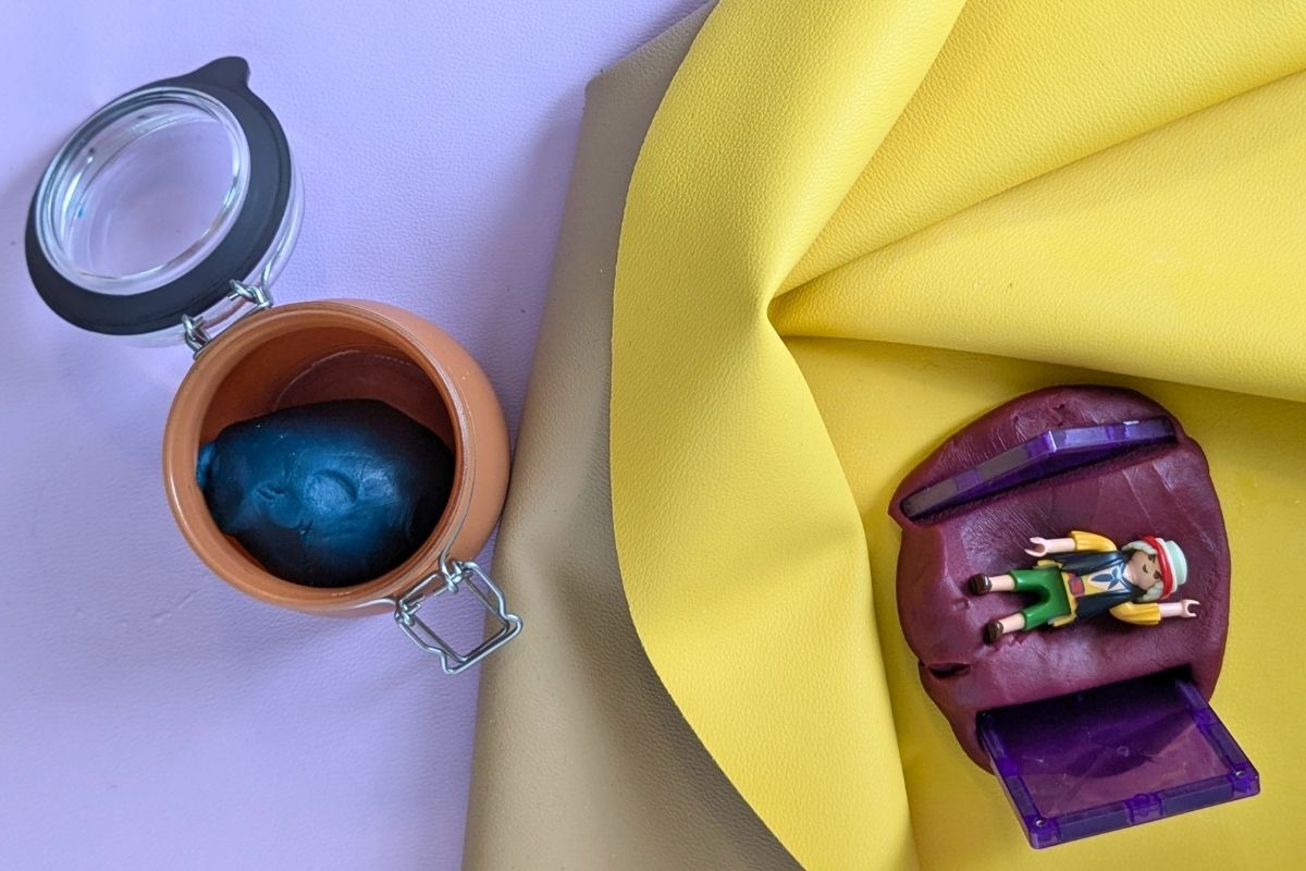 Small Playmobil toy figure resting on homemade playdough on a yellow Huske mat