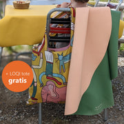 LOQI tote bag illustrated by Clara San Millán hanging on a chair beside a peach and green Huske mat, free with the pair until 15 November