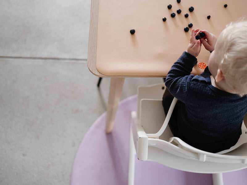Child playing at a table on a silicone leather play mat, enjoying sensory activities in a modern setting.