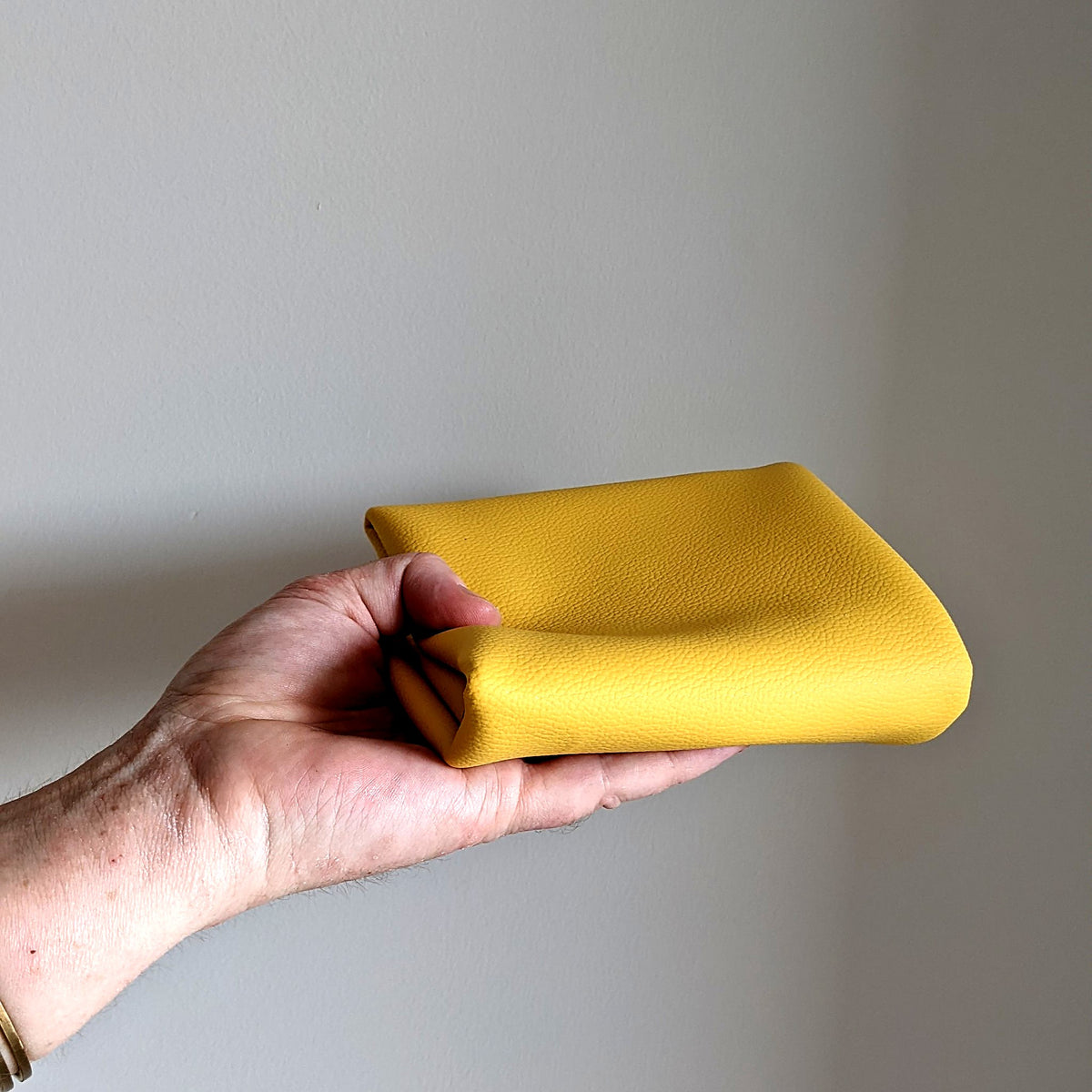 Roam Round Yellow/Mocca silicone splat mat folded into a small bundle that sits in one hand