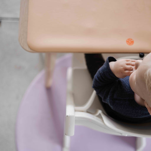 Roam Round Lilac/Red silicone splat mat, child at the high chair with the round mat on the floor beneath