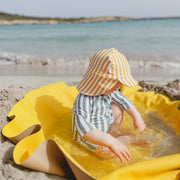 Roam Round Yellow/Mocca silicone splat mat, child sitting on the round mat at the water edge
