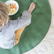 Roam Round Peach/Green silicone splat mat, child stretched out on the round mat beside a plate of fruit