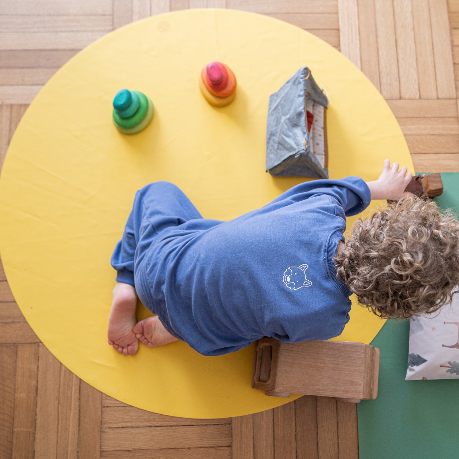 Roam Round Yellow/Mocca silicone splat mat, toddler playing with stacking toys on the yellow round mat
