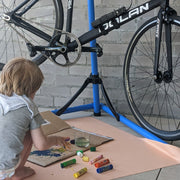 Roam Square Peach/Green silicone craft mat, young boy sitting on blush huske mat painting on cardboard with colourful
