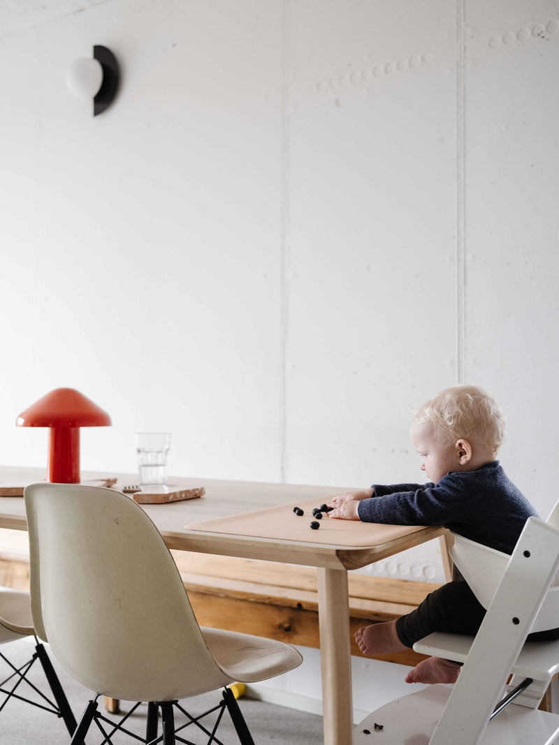 Toddler in a high chair with a peach Huske mat on the table and a lilac round mat on the floor