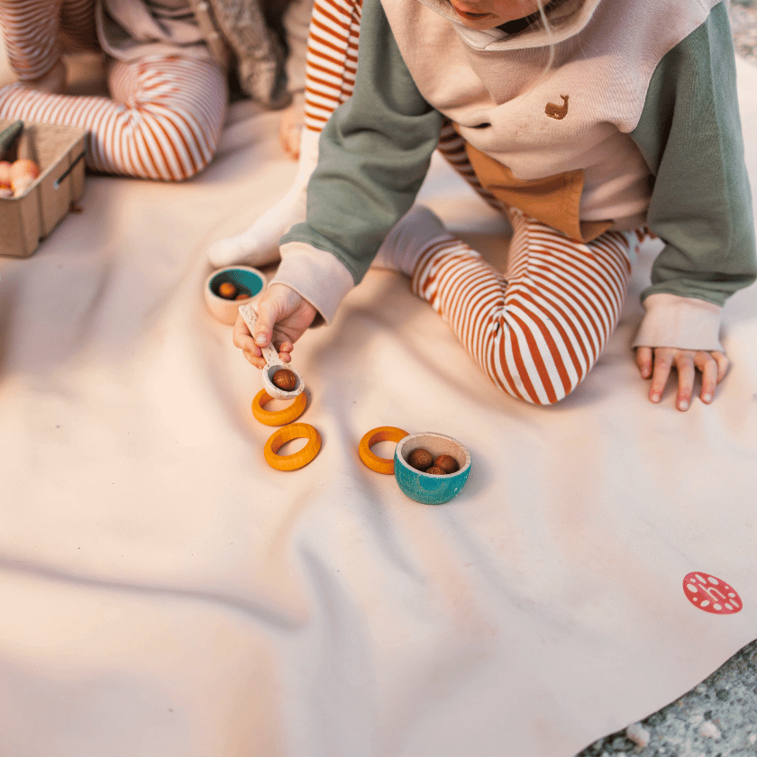 Young children and toddlers sitting and playing on a studio huske gallivant picnic mat on the beach while on holiday